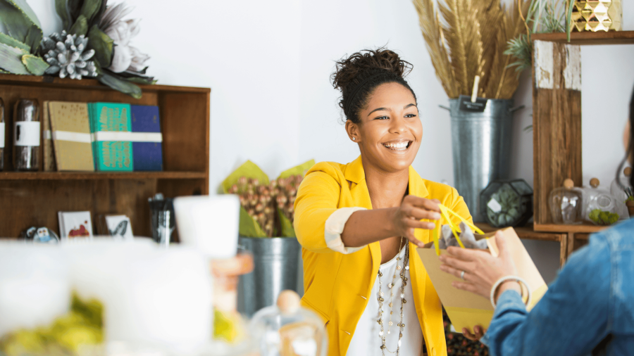 A woman behind a counter handing a bag to a customer.