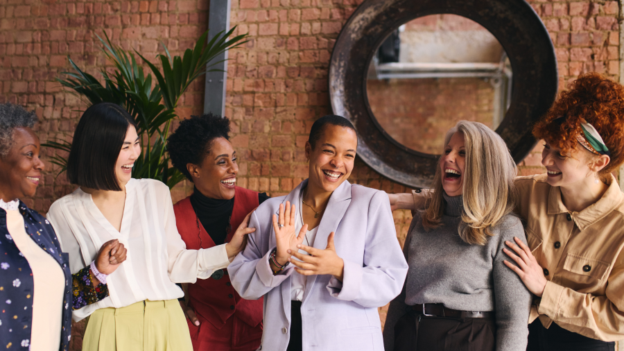 A diverse group of women standing around smiling and laughing.